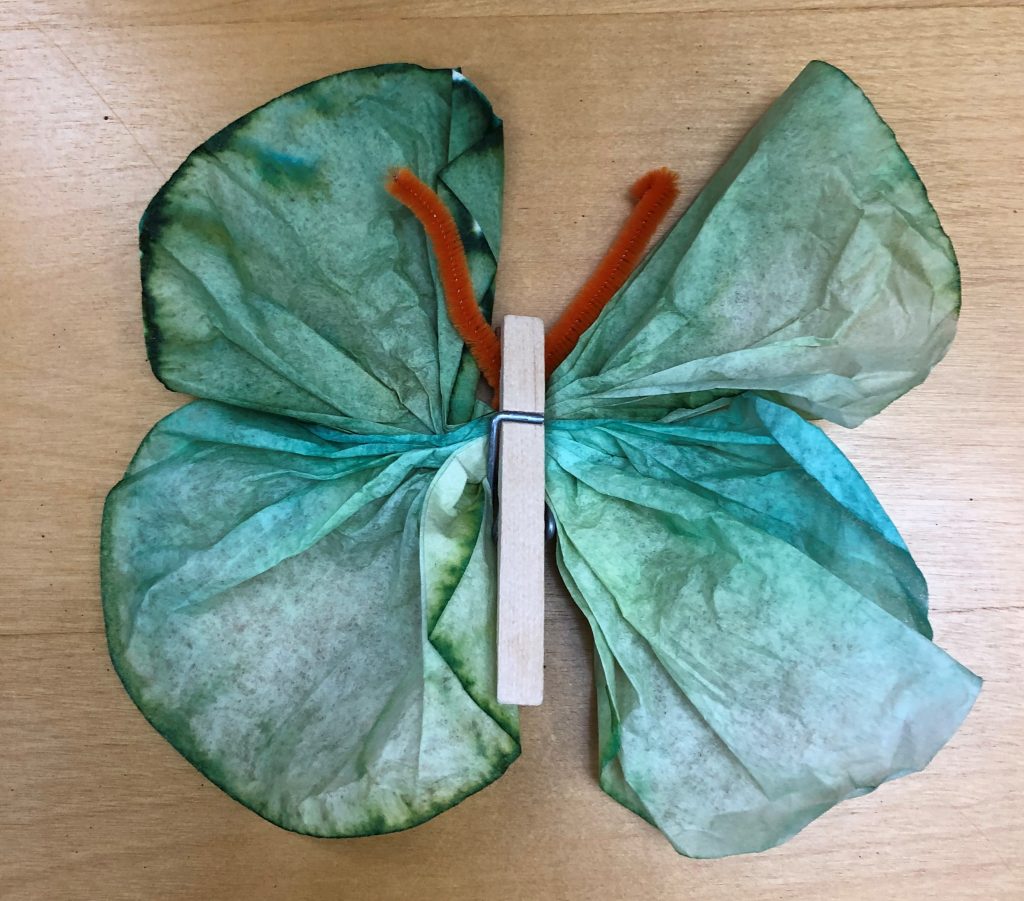 A photo of a butterfly made from a clothespin, pipe cleaner, and colored coffee filter.