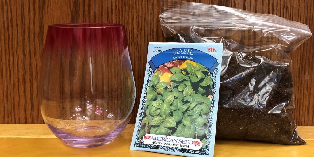 A photo of a plastic stemless wine glass, a packet of seeds, and a bag of soil.